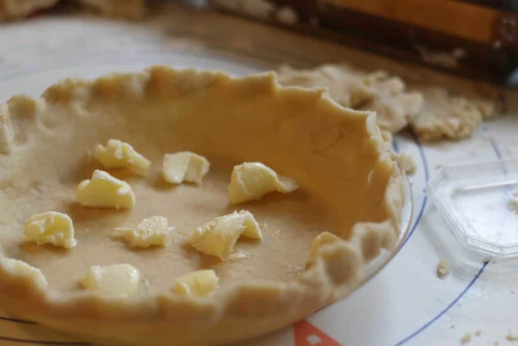 An unbaked pie shell with dots of butter on it.