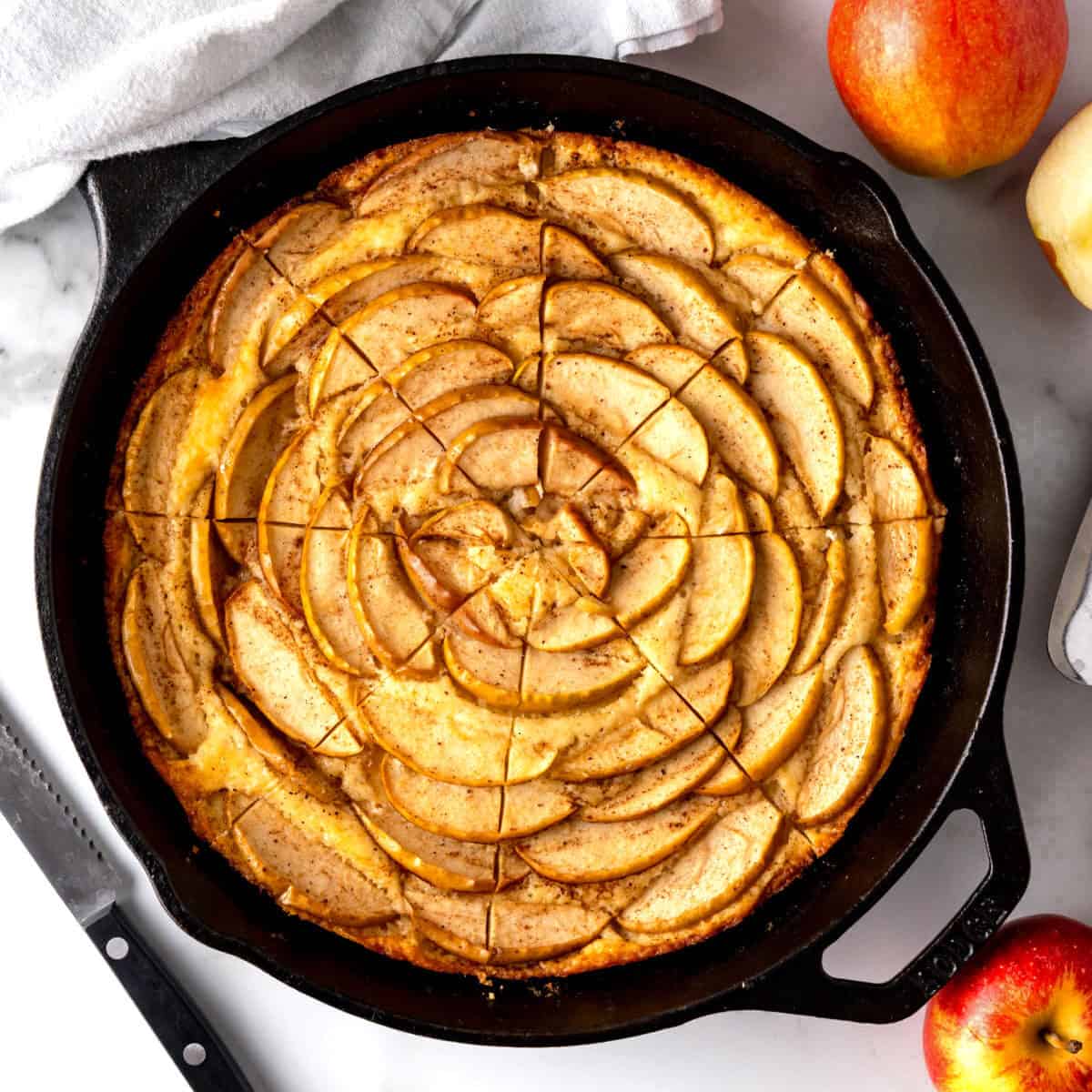 A slice skillet cake with apples in an iron pan.