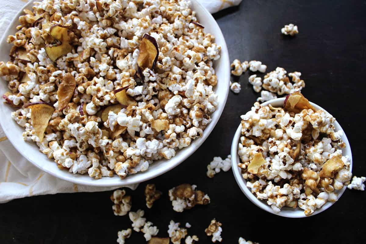 Caramel coated popcorn with apples on top in a white bowl.