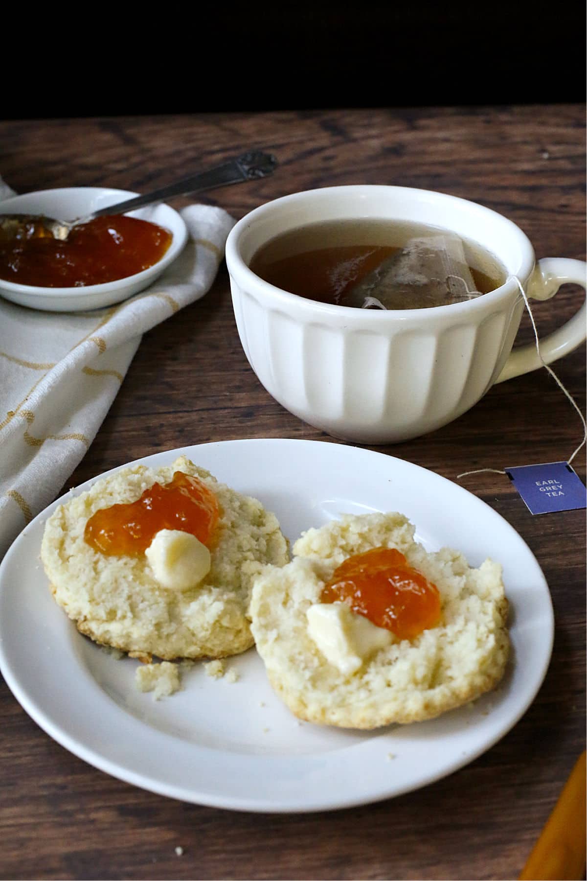 A cup of tea with biscuits with butter and jam.