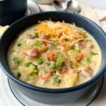 A bowl of potato chowder with ham and cheese.