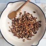 Pecans in a skillet with a wooden spoon.