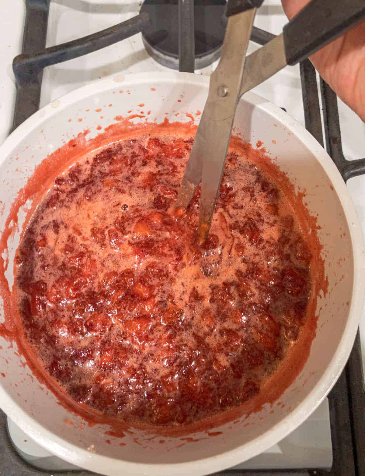 Using scissors to cut up strawberries in a saucepan.