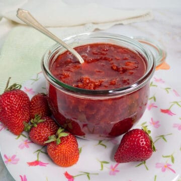 Strawberry preserves in a glass jar with a spoon.