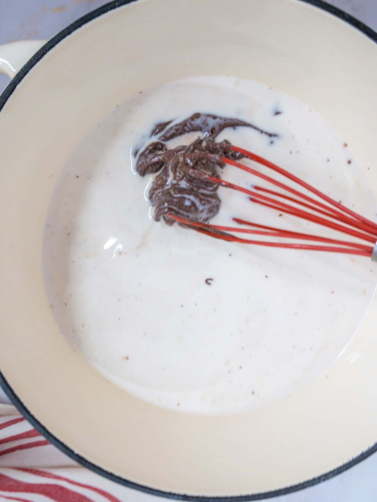 Whisking chocolate into milk in a saucepan.