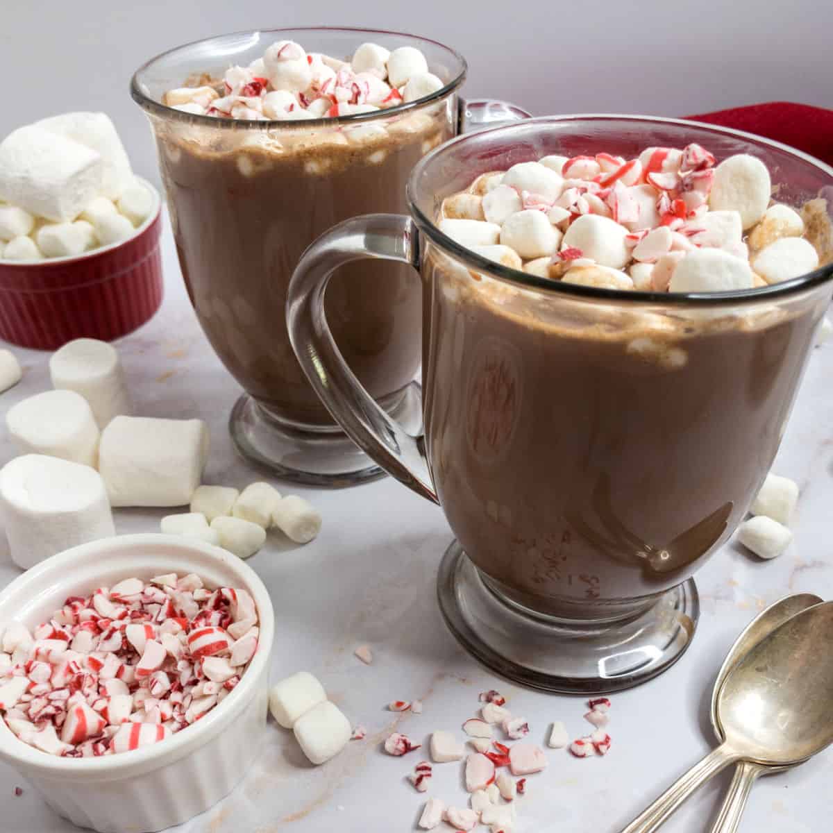 Two mug of cocoa with marshmallows and peppermint candies.