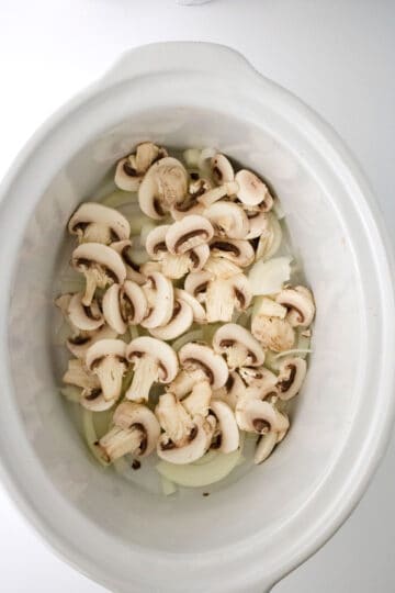 Sliced mushrooms in a white crock pot.