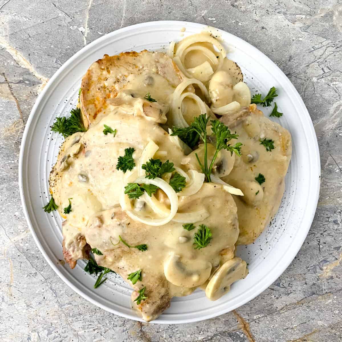Pork chops in mushroom soup on a white plate.