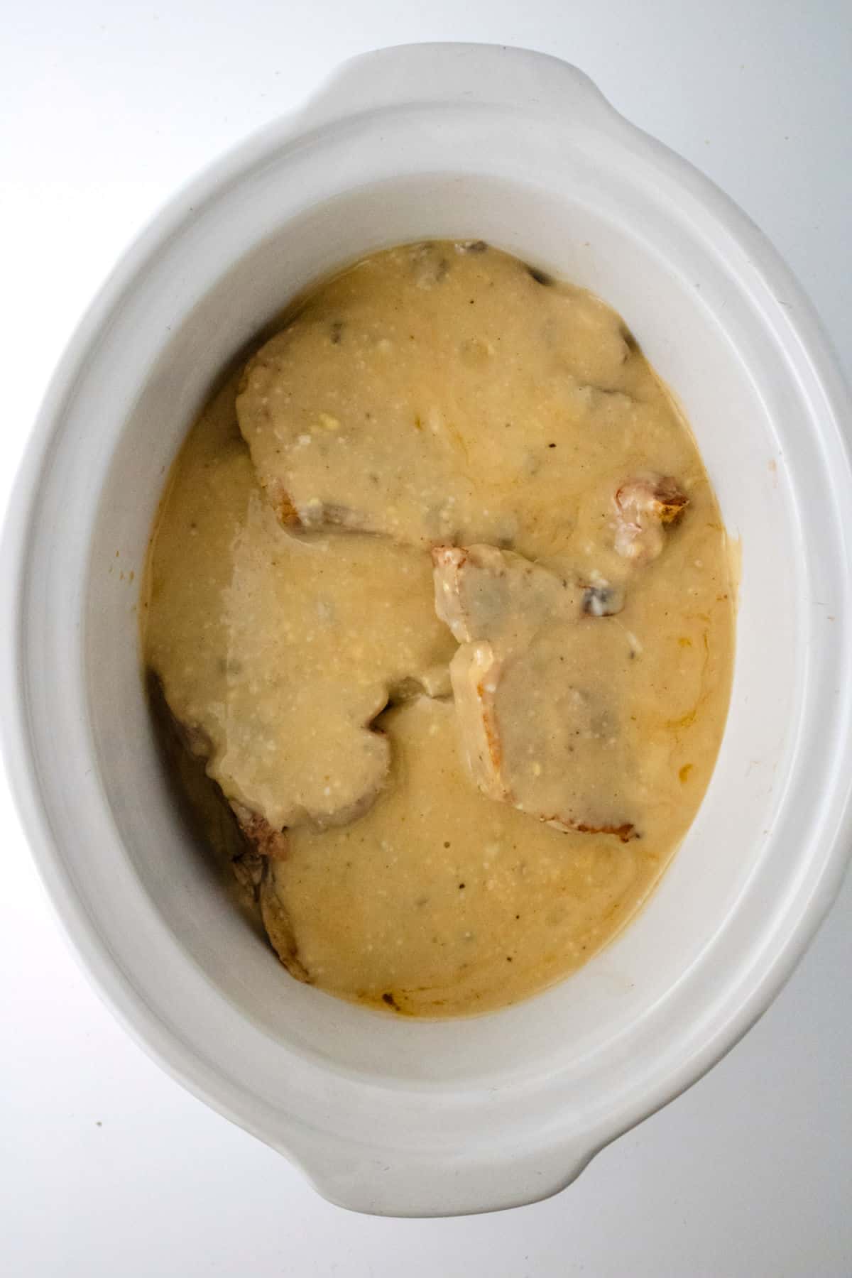 Pork chops topped with gravy in a white crock pot.