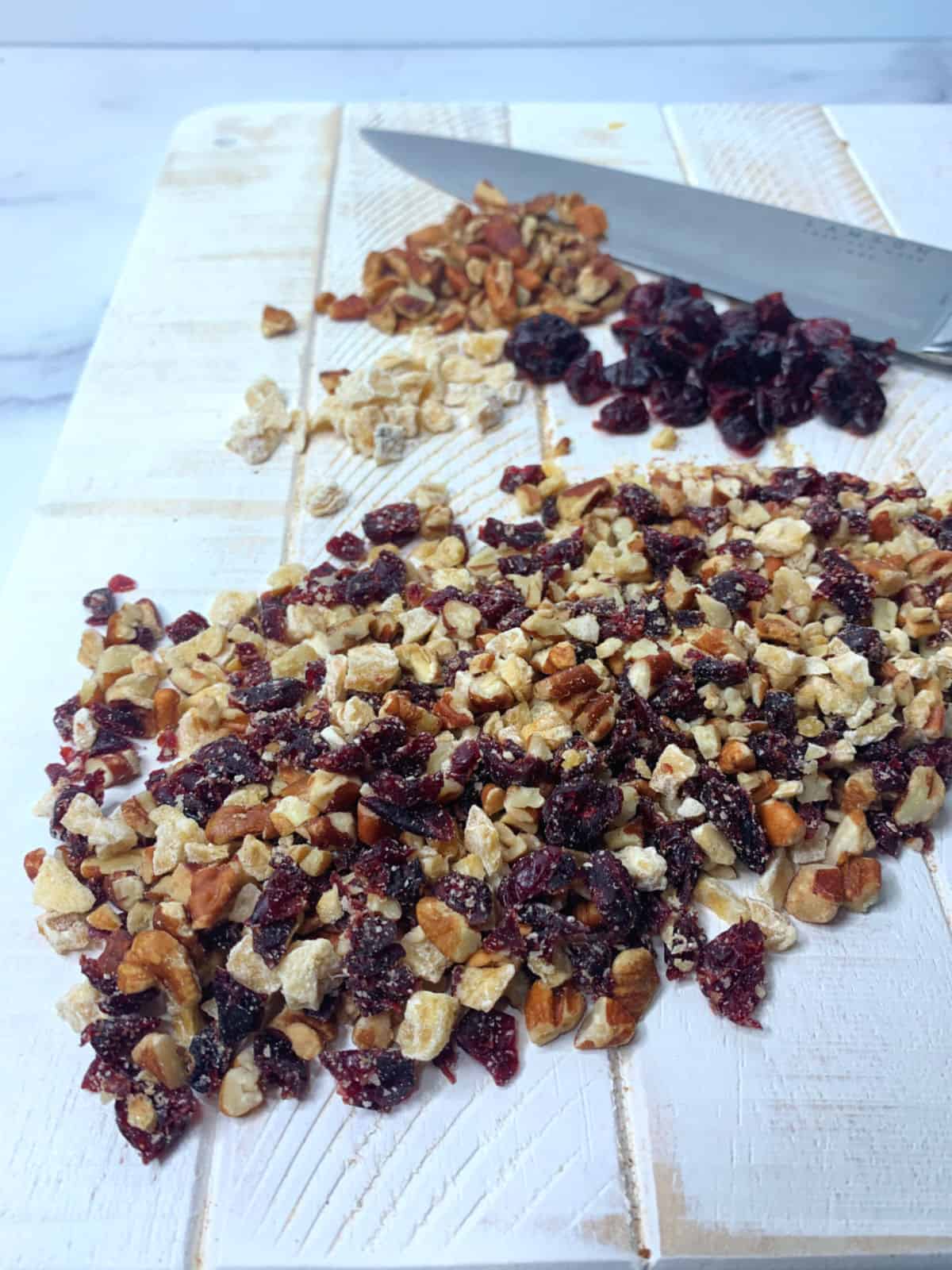 Chopping ginger, cranberries and pecans all together on a white board.