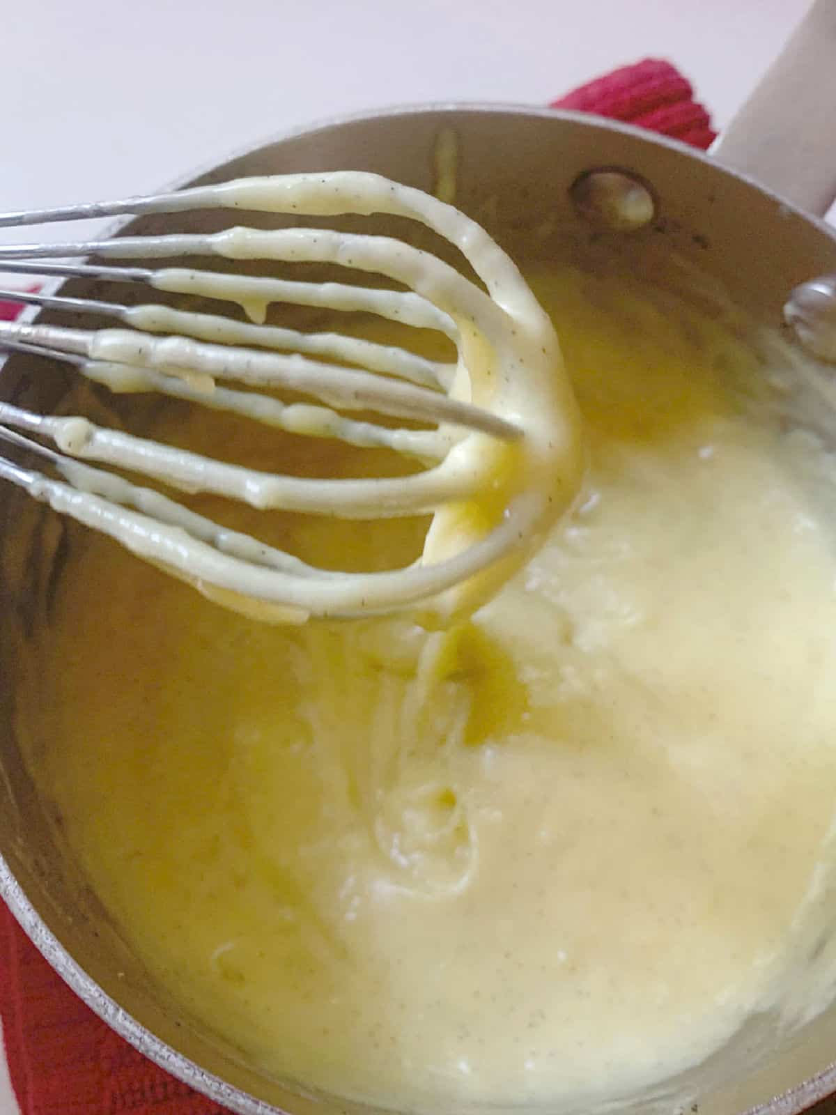 A saucepan with cooked custard and a whisk.