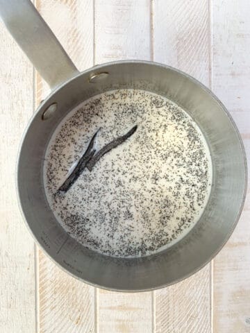 A saucepan with milk and vanilla bean seeds and the vanilla bean pod on a white board.