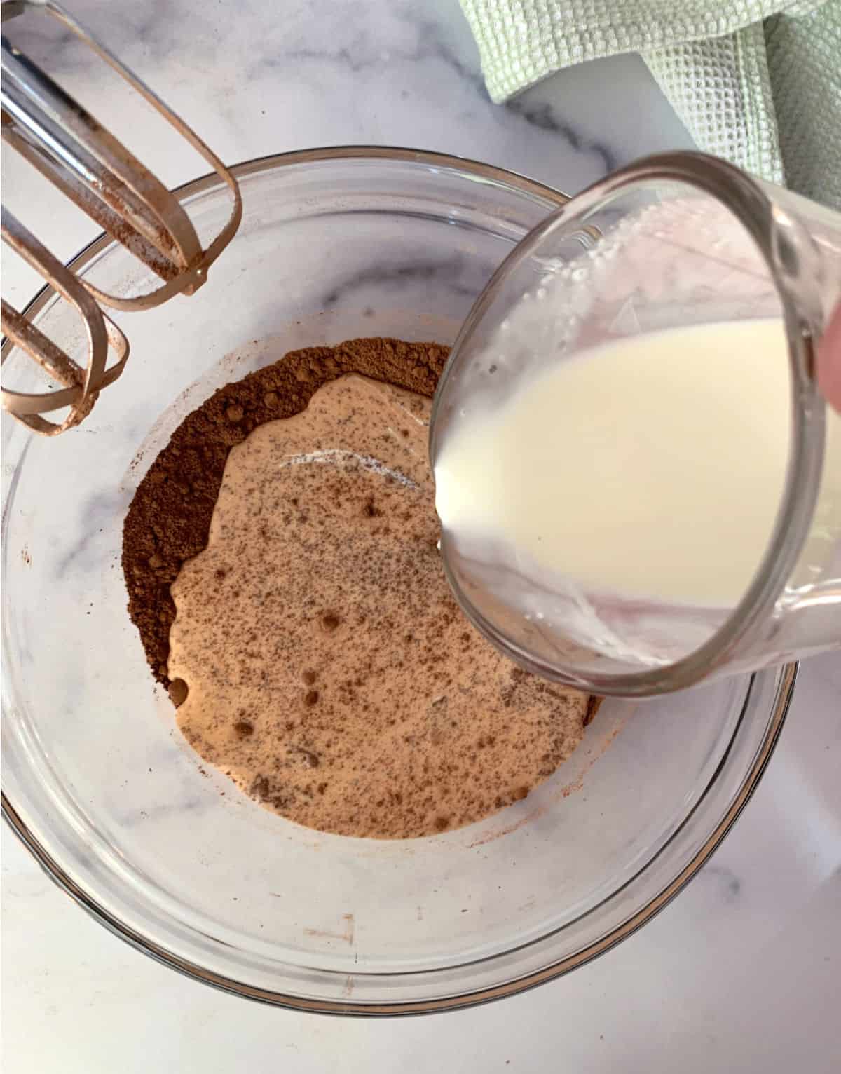 Adding cream to cocoa powder in a glass mixing bowl.