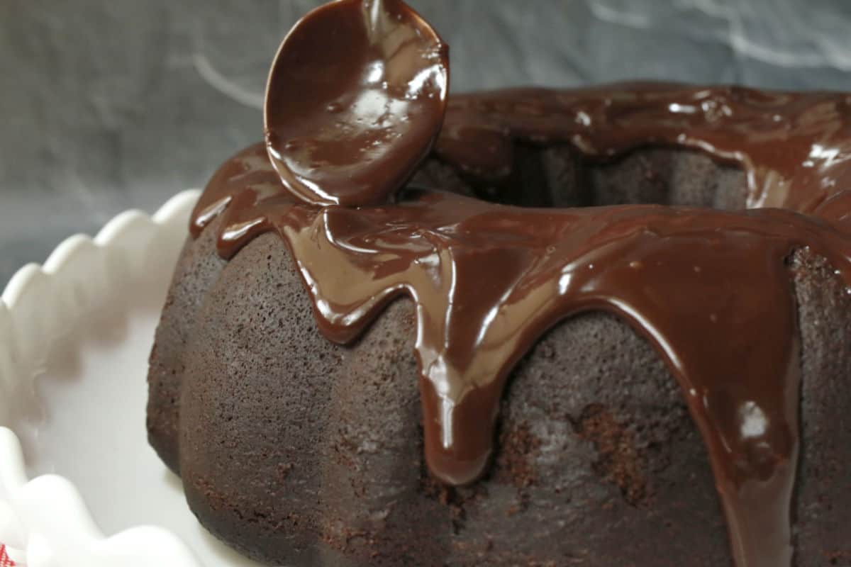 Spooning chocolate ganache on a chocolate cake.
