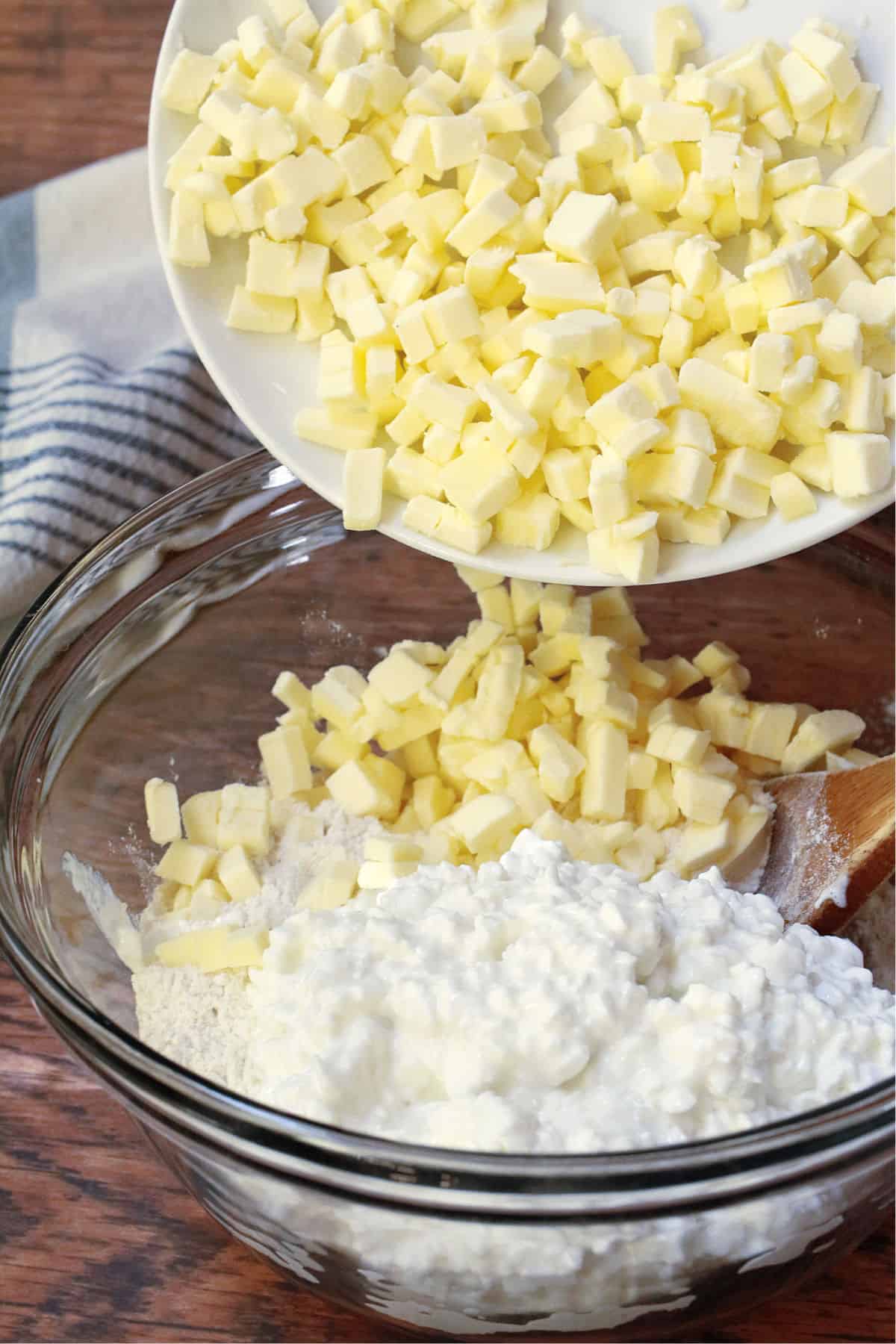 A clear glass bowl filled with cottage cheese and flour, and adding cubed butter.