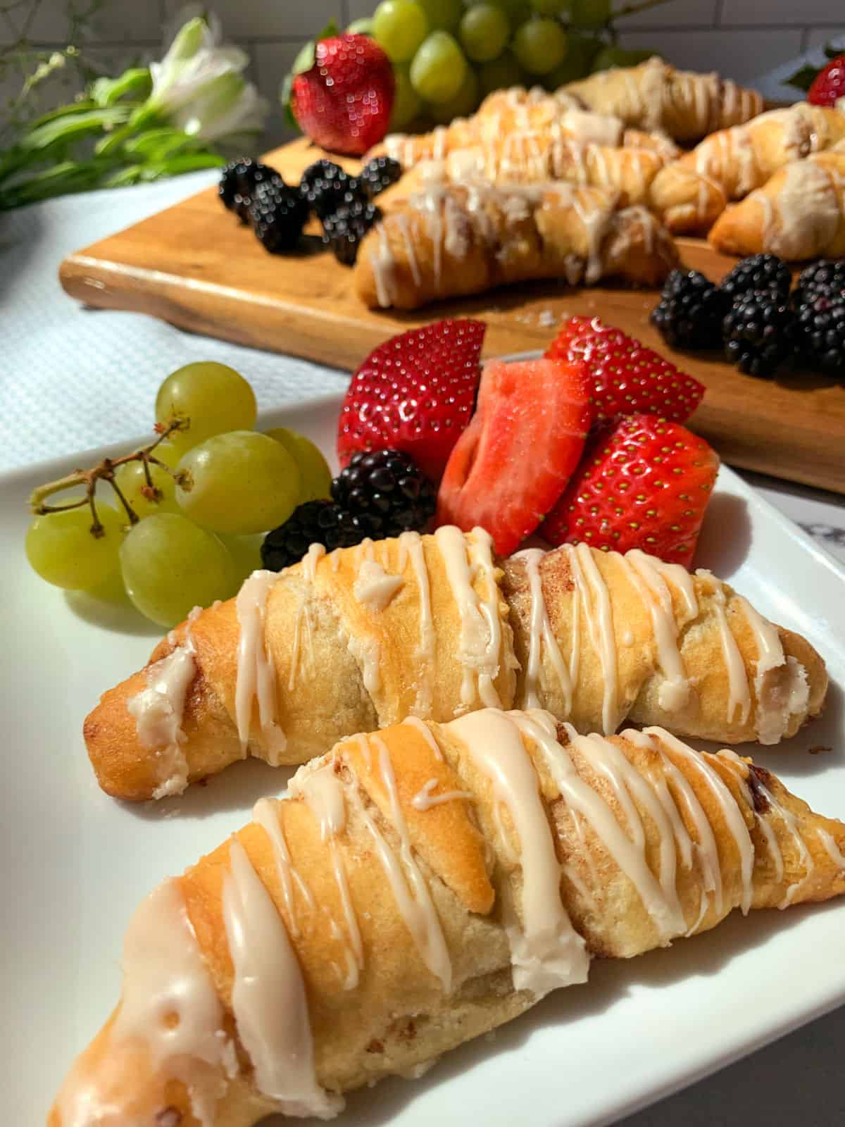A white plate with crescent rolls on it along with strawberry, blackberries and grapes.