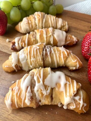 Cinnamon roll crescent with icing, sitting on a wood board.
