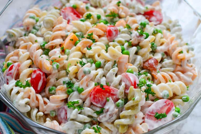 Pasta salad with tomatoes, cheese and bacon in a glass bowl.