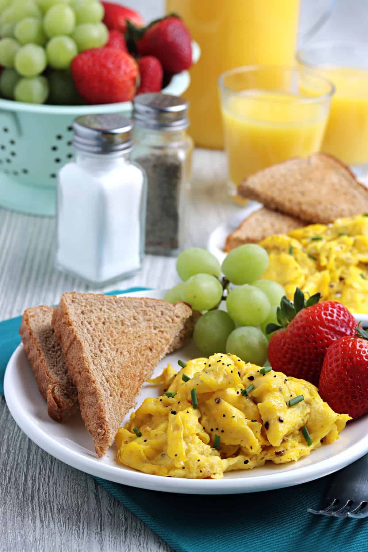 Scrambled eggs on a white plate with toast and fruit.