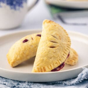 A white plate with three baked cherry hand pies.