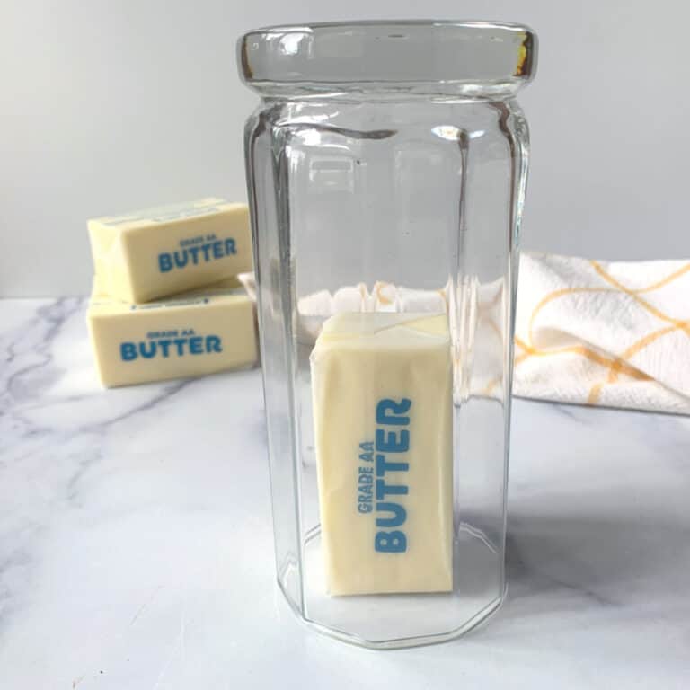 A clear drinking glass set over a stick of butter, with sticks of butter in the background.