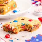 M&M cookies on a white plate with a bite taken out of it.