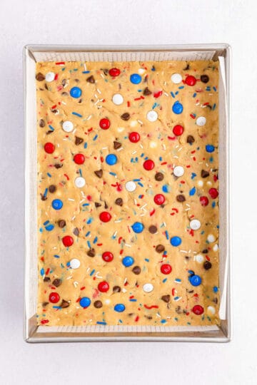 Raw cookie dough with red, white and blue M&M and sprinkles. in a baking pan.