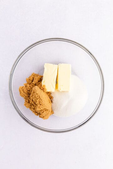 White sugar, brown sugar and butter in a clear glass bowl.