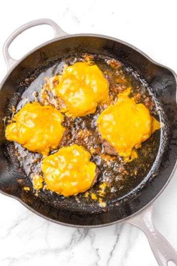 Melted cheese on hamburgers in an iron skillet.