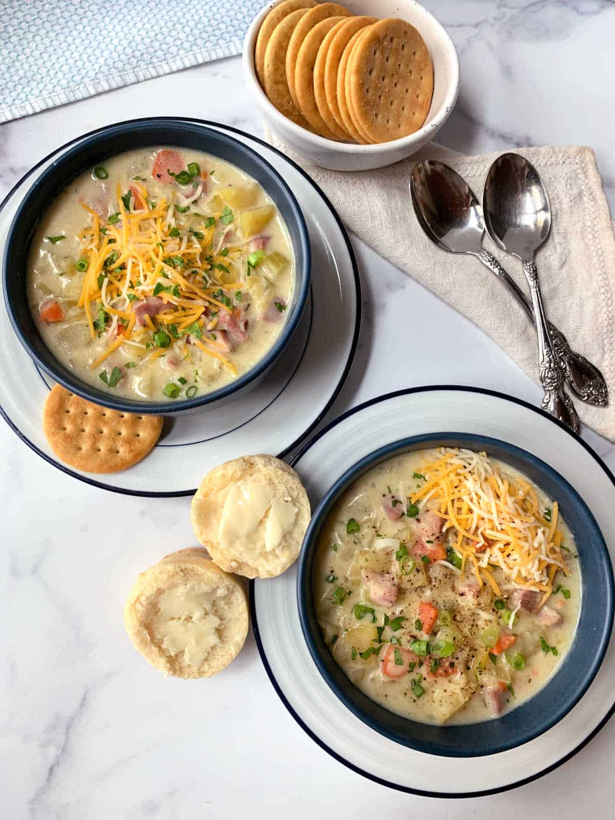 Two bowls of ham soup with crackers and biscuits.