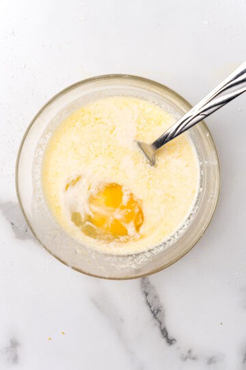 A glass bowl with an egg, orange juice and milk.