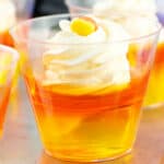 A group of small cups with whipped cream and candy corn in them.