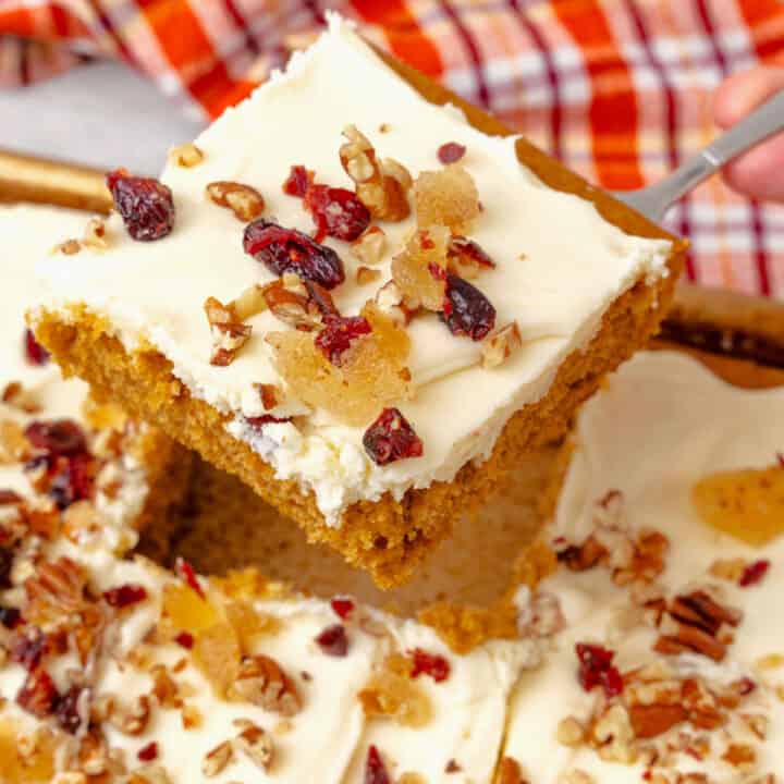 A slice of pumpkin cake with white icing and a fruit and nut topping.
