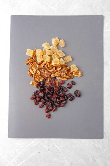A cutting board with ginger, pecans and cranberries on it.