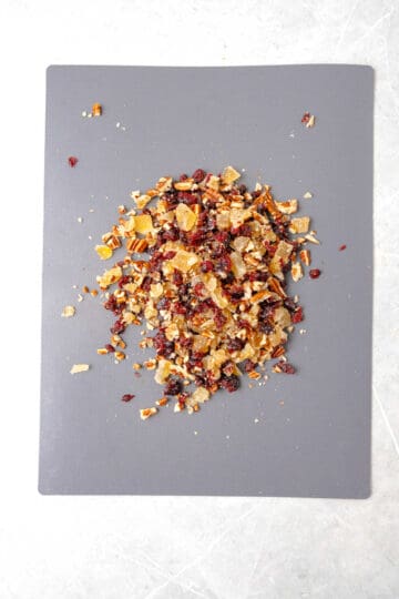 A chopped dried cranberries pecans and ginger on a gray surface.