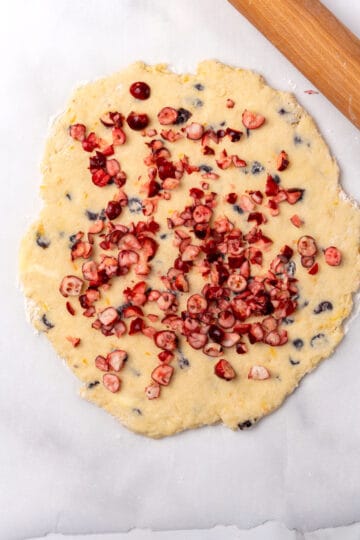 A scone dough with cranberries and a rolling pin.