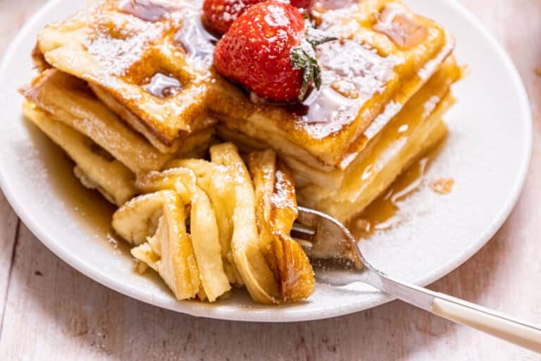 Waffles with strawberries and syrup on a plate with a fork.