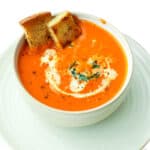 A bowl of tomato soup with croutons on top.