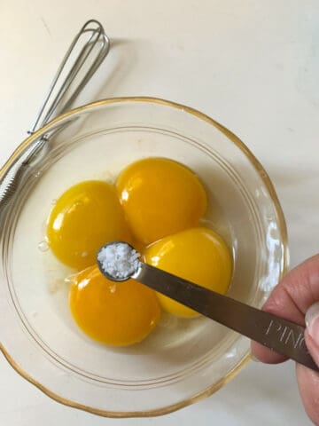 A person is mixing eggs in a bowl with a whisk.