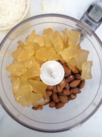 A food processor filled with almonds and candied pineapple.