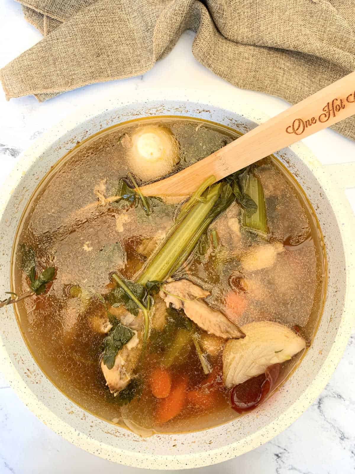A bowl of soup with vegetables and a wooden spoon.