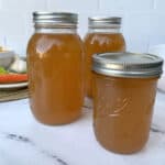 Three mason jars of chicken broth on a counter.