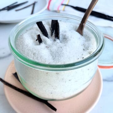 Vanilla ice sugar in a jar with a spoon on a pink plate.