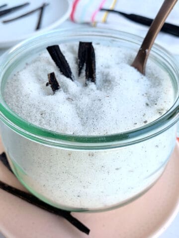 Vanilla ice sugar in a jar with a spoon on a pink plate.