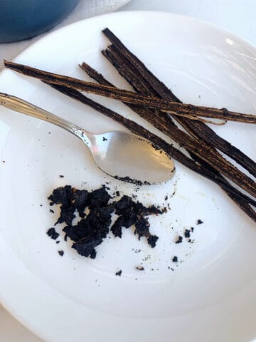 A white plate with vanilla bean pods and a spoon.