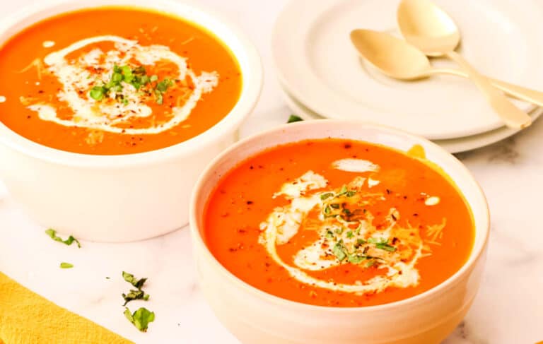 Two white bowls of tomato basil soup.