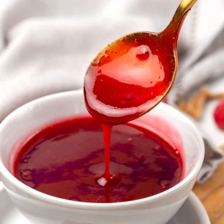A spoon is pouring raspberry sauce into a bowl.