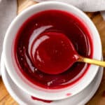 Raspberry sauce in a white bowl with a spoon.