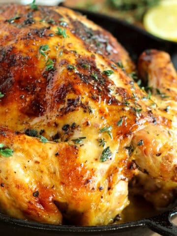 A roasted chicken in a cast iron skillet with lemons.