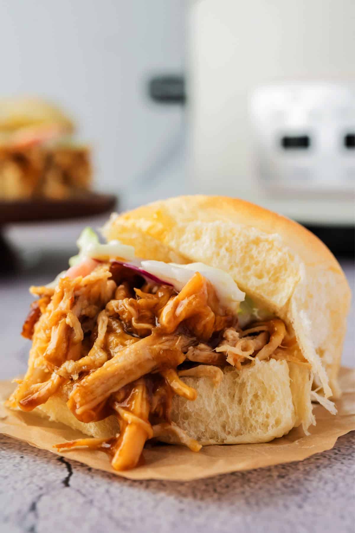 A close-up of a pulled pork sandwich on a bun, topped with coleslaw.